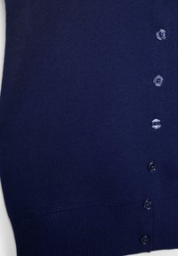 Granatowa dzianina z sześcioma ciemnoniebieskimi guzikami ułożonymi pionowo i ściągaczem u dołu.