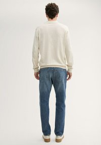 Ljusbeige långärmad polo t-shirt med ribbade manschetter, tillsammans med medelblå jeans. Outfitten har bakfickor och en avslappnad passform.