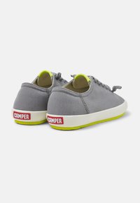 Sneakers in tela grigia con profilo basso, forma arrotondata, suola gialla brillante e logo rosso "CAMPER" sul tallone.