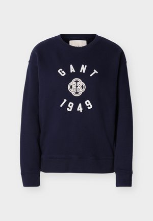 Marineblå crewneck-genser med hvit GANT-logo, sirkulært emblem og "1949" trykt på forsiden, lange ermer, ribbede mansjetter og kant.