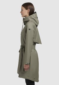 Olive green waterproof trench coat with a hood, belted waist, and buttoned cuffs. Features a distinctive logo on the sleeve.