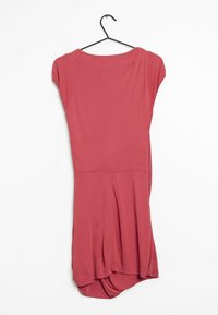 Kortärmad klänning i dammig rosa med ett mjukt tyg, avslappnad passform och rundad fåll. Hänger från en svart krok.