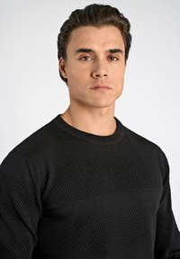 Czarny sweter z teksturowymi poziomymi paskami, okrągłym dekoltem i ściągaczami. Gładki materiał o subtelnym wzorze.