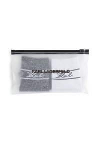 Deux paires de chaussettes dans une pochette en plastique transparente. Une paire est noire, l'autre est blanche, toutes deux avec des rayures noires et des accents de logo écrits.