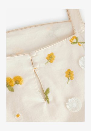 Kreemikatne, millel on kollased ja valged lilleline tikand. Seljal on nööpdetail ja õrn pitsääris rihmadel.