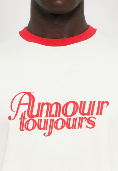 Hvid bomulds T-shirt med en kontrastfarvet rød ribbet halsudskæring. Har fed rød tekst, der siger "Amour toujours" i en dekorativ skrifttype.