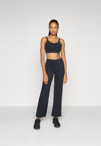 Zwart atletisch outfit bestaande uit een cropped tanktop en hoge, uitlopende broeken, gemaakt van een glad, rekbaar materiaal, gecombineerd met zwarte sneakers.