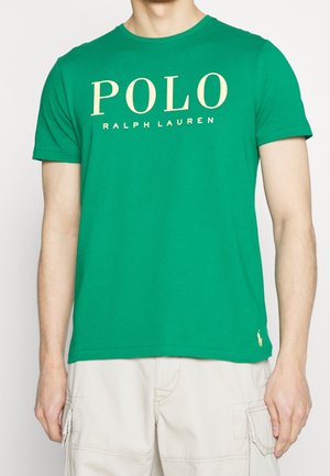 Mand iført en grøn T-shirt med korte ærmer med teksten "POLO RALPH LAUREN", kombineret med lyse beige cargoshorts.