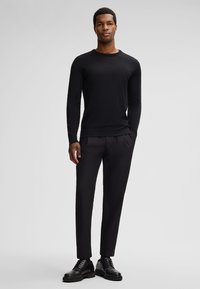 Slim-fit zwarte lange mouwen shirt gemaakt van een glad materiaal, gecombineerd met zwarte geplooide broeken en zwarte veterschoenen.
