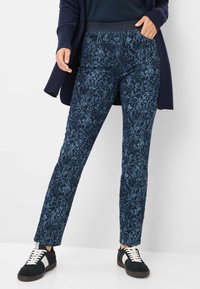 Donkerblauwe broek met een een gestructureerd bloemenpatroon, voorzien van een rekbare tailleband en zijzakken, gecombineerd met zwarte sneakers.
