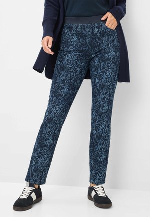 Donkerblauwe broek met een een gestructureerd bloemenpatroon, voorzien van een rekbare tailleband en zijzakken, gecombineerd met zwarte sneakers.