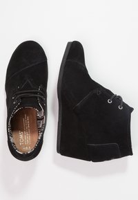 Stivaletti neri in suede con tacco a zeppa, dotati di chiusura con lacci, interno testurizzato e dettagli di cucitura discreti.
