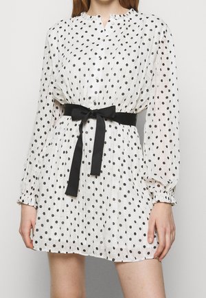 Biała mini sukienka z długim rękawem w czarne kropki, zapinana na guziki, z falbankami na mankietach i czarnym paskiem wiązanym w talii.