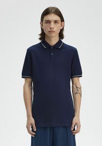 Polo de color marino hecho de tela texturizada, con un cuello con dos botones, puños a rayas en contraste y un pequeño logotipo bordado en el pecho.