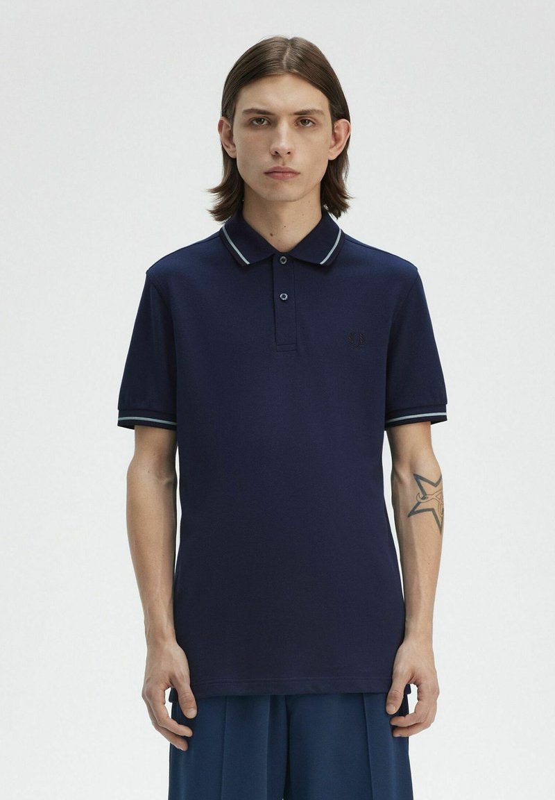 Polo de color marino hecho de tela texturizada, con un cuello con dos botones, puños a rayas en contraste y un pequeño logotipo bordado en el pecho.
