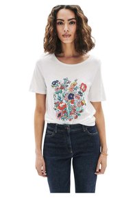 Witte t-shirt met korte mouwen, versierd met een kleurrijke bloemenprint in rood, blauw en groen. Gecombineerd met hooggetailleerde donkere denim jeans.