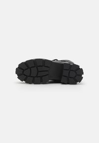 Black boot sole with rugged tread pattern, designed for grip. Material appears rubber with a textured surface. Flat heel and reinforced edges.