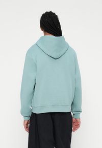 Sudadera azul claro con una capucha estructurada, corte holgado, puños y dobladillo de canalé. La parte posterior presenta costuras limpias y una textura suave.
