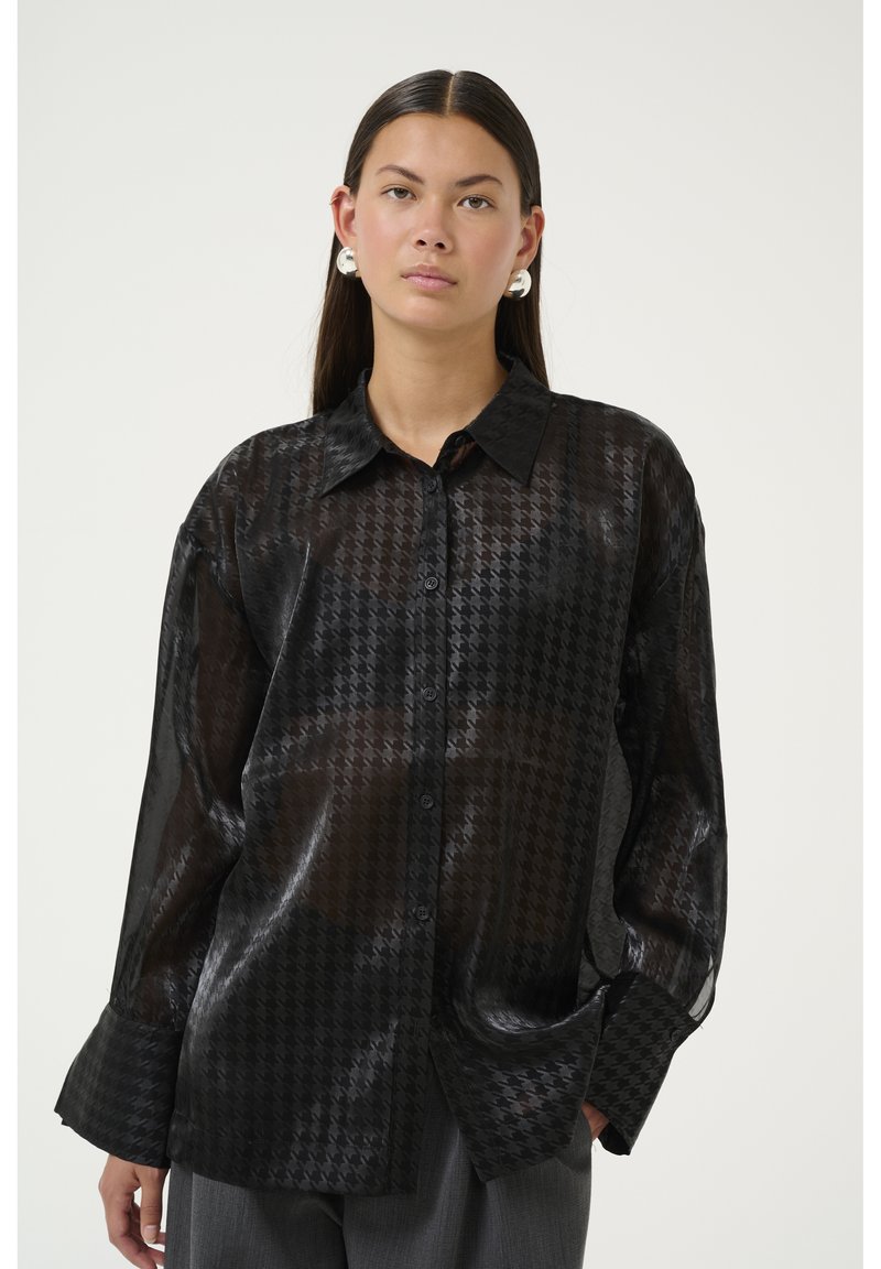 Sort, gennemsigtig skjorte med knapper og houndstooth-mønster, lange ærmer og klassisk krave. Materialet har en glat, let glansfuld tekstur.