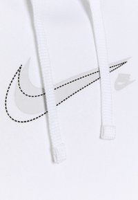 Vit hoodie med grå Nike-logotyp; har en sydd kontur, dragsnören och ett strukturerat tyg. Minimalistisk design, inga mönster eller accenter.