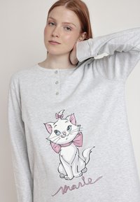Camisa de manga larga gris con cuello tipo henley y tres botones, que presenta una ilustración de un gato de dibujos animados con un lazo rosa y el nombre "Marie".