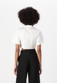 Blusa blanca cortada con mangas cortas y cuello, combinada con pantalones negros de tiro alto. Tejido suave y ajuste entallado.