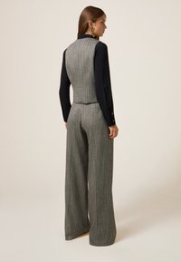 Grijze geblokte vest en bijpassende broek met brede pijpen, gemaakt van gestructureerde stof, met een zwart langemouwen shirt eronder en gouden hardware accenten.