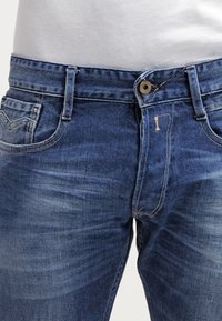 Blå denimjeans med en bleknad finish, med knappstängning, framfickor och synliga sömdetaljer.