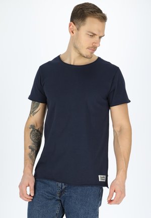 Marineblå bomulds T-shirt med korte ærmer, rund halsudskæring og lille logo patch på den nederste kant. Båret med denim jeans.
