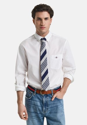 White long-sleeve shirt with a breast pocket, paired with a striped blue and gray tie. Worn with blue jeans and a brown belt.