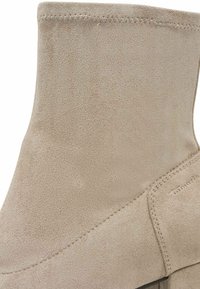 Zbliżenie beżowego zamszowego botka za kostkę, pokazujące szczegółowe szwy i gładką fakturę.