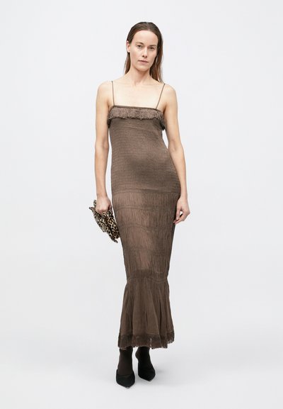 Barna kötött maxiruha a felsőrésznél és az alján rojttal, testhez simuló fazonban, vékony spagettipántokkal és A-vonalú szoknyával.