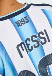 Zadní strana modro-bílého pruhovaného sportovního dresu s potiskem „1893“ a „MESSI“, nošeného osobou s tetováním na krku „SAUDADE“.