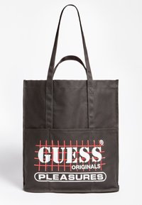 Sac fourre-tout en tissu noir avec deux longues poignées, présentant un motif à carreaux rouges et un texte imprimé en blanc "GUESS ORIGINALS PLEASURES" à l'avant.