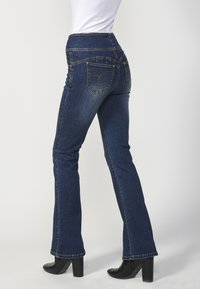 Jean évasé en denim bleu foncé avec une taille haute, des coutures contrastantes et deux poches arrière ornées de décorations.