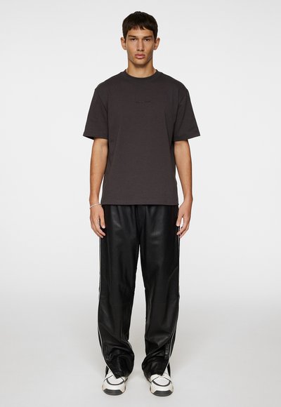 Mörkgrå bomullströja med rund hals och korta ärmar, kombinerad med svarta byxor i konstläder med vita sidostråk.