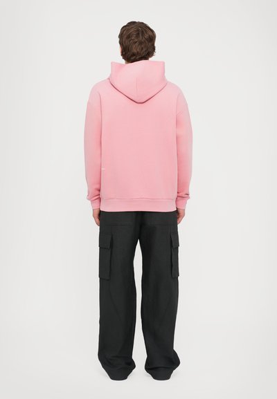 Sweatshirt à capuche rose clair avec une coupe décontractée, des poignets et une taille côtelés, associé à un pantalon cargo noir avec de multiples poches.