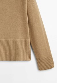Manche de pull beige tricoté et ourlet inférieur avec poignets et ceinture côtelés sur fond blanc.