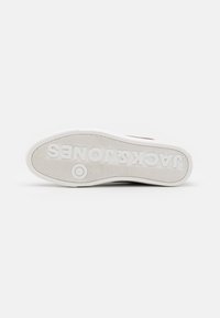 Semelle de sneaker blanche avec un motif de semelle texturé. Présente "JACK & JONES" embossé sur la semelle extérieure. Matériau en caoutchouc lisse avec une forme arrondie.