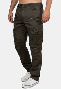 Olivgrüne Cargo-Hosen mit mehreren Reißverschlusstaschen, strukturierten Kniepaneelen und taillierter Passform. Dazu weiße Sneaker.