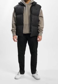 Czarna kamizelka puchowa na szarym hoodie, zestawiona z czarnymi spodniami cargo i białymi trampkami. Kamizelka ma zamek błyskawiczny i kaptur.