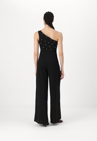 Black jumpsuit with an asymmetrical one-shoulder design, embellished with white pearl details; wide legged silhouette made of smooth fabric.
