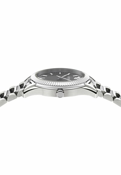 Montre-bracelet en métal argenté avec une lunette rainurée et un bracelet à maillons, vue de profil montrant la couronne et le cadran plat.