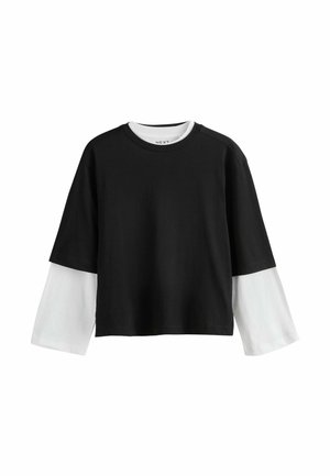 Juoda trumpa ilgarankovė palaidinė suapvalintu kaklu, dėvima ant baltos palaidinės ilgomis rankovėmis, rodoma ant vientisos baltos fono.