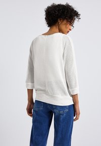 Witte, lichtgewicht gebreide trui met een textuurpatroon, driekwartmouwen en een relaxed fit, gecombineerd met blauwe spijkerbroek.