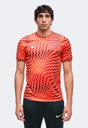 Ung mand iført en rød og orange zigzagmønstret sportstrøje med det tyrkiske flag og sorte bukser med en gul Nike-logo.