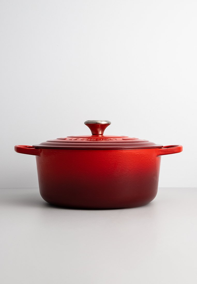 Roter Gusseisen-Topf mit strukturiertem Finish, einem Edelstahlknopf und zwei gebogenen Griffen. Runde Form, beträchtliche Größe und geprägtes Deckeldesign.