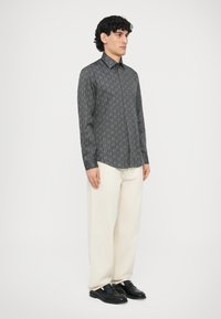 Czarna koszula w wzory z długim rękawem i kołnierzykiem, zestawiona z kremowymi szerokimi spodniami i czarnymi butami, o gładkiej fakturze.