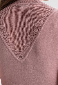 Retro di un maglione a maglia malva con un pannello triangolare texturizzato caratterizzato da un motivo floreale in rilievo.