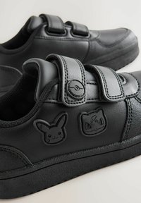 Chaussures en cuir noir avec surface texturée, dotées de bandes Velcro et de détails en relief des personnages Pokémon : Pikachu et Bulbizarre. Semelle plate.